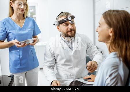 Patienten mit Senior otolaryngologist und weibliche Hilfskraft in der HNO-Büro während einer medizinischen Untersuchung Stockfoto