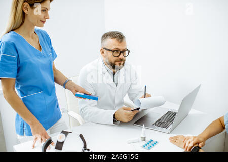 Junge Patienten an einen Termin mit otolaryngologist und sein Assistent, Sitzen während der Beratung in der hellen HNO-Büro innen Stockfoto