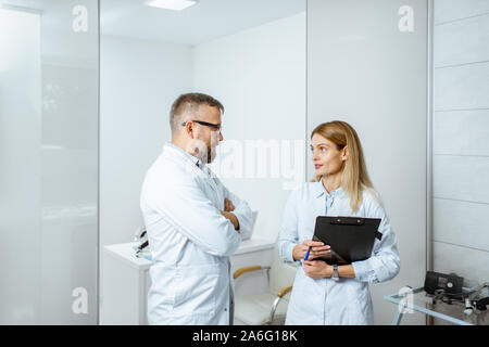Zwei ältere Ärzte sprechen beim zusammen im Krankenhaus stehen während einer medizinischen Konferenz Stockfoto