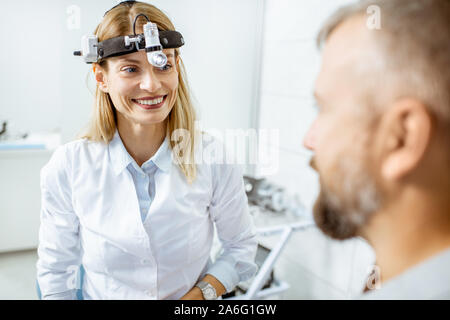 Portrait einer weiblichen zuversichtlich Otolaryngologist während einer medizinischen Beratung mit erwachsenen Patienten an der HNO-Büro Stockfoto