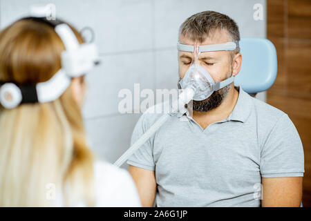 Erwachsenen Mann Atmung während einer medizinischen Behandlung mit Atemschutzmaske gegen Schnarchen sitzen mit Arzt an der HNO-Büro Stockfoto