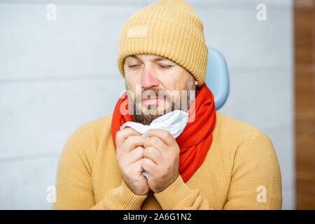 Porträt eines erwachsenen Patienten Übelkeit, sitzen in warme Kleidung mit laufender Nase an der medizinischen Büro Stockfoto