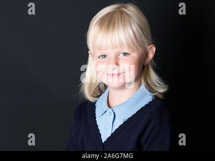 Ein wunderschönes kleines Mädchen stellt für die Schule eine einheitliche Bilder auf schwarzem Hintergrund, für das neue Schuljahr bereit, neutralen einheitlichen, blaue und weiße prüfen Stockfoto