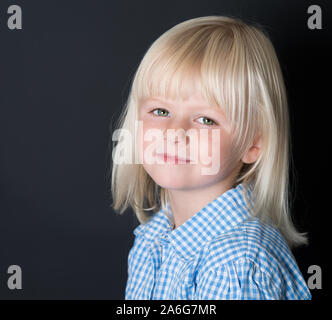 Ein wunderschönes kleines Mädchen stellt für die Schule eine einheitliche Bilder auf schwarzem Hintergrund, für das neue Schuljahr bereit, neutralen einheitlichen, blaue und weiße prüfen Stockfoto