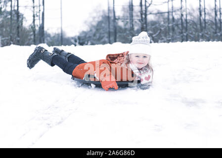 Ein wunderschönes kleines Mädchen mit einem roten Mantel und Wooly hat im Schnee spielen an einem kalten Wintertag an Weihnachten, Heiligabend, Trentham Gardens, Stoke Stockfoto