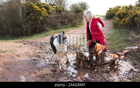 Hübsches kleines Mädchen springen in sehr schlammigen Pfütze das Spielen mit Ihrem Hund in der kalten Herbst Wetter in Stoke-on-Trent, Staffordshire Stockfoto