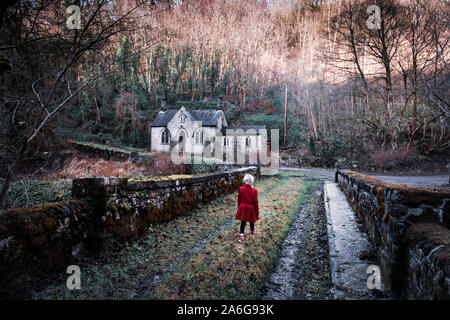 Ein kleines Mädchen auf dem Weg zu einem alten verlassenen Haus furchtsam, Spooky, Kirche im Wald, in der Derbyshire Peak District National Park, heiliget Stockfoto