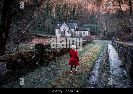 Ein kleines Mädchen auf dem Weg zu einem alten verlassenen Haus furchtsam, Spooky, Kirche im Wald, in der Derbyshire Peak District National Park, heiliget Stockfoto