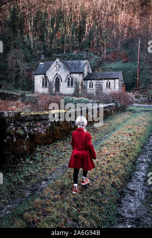 Ein kleines Mädchen auf dem Weg zu einem alten verlassenen Haus furchtsam, Spooky, Kirche im Wald, in der Derbyshire Peak District National Park, heiliget Stockfoto