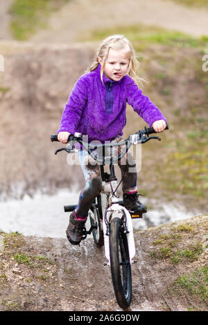 Ein hübsches kleines Mädchen mit blonden Haaren und einem lila Jumper genießt einen Tag an einem BMX-Bahn, Reitschule und Üben von Tricks, Kind auf dem Land Großbritannien Stockfoto