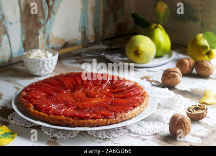 Quitte Tarte Tatin mit Schlagsahne, Quitte Obst und Walnüsse auf einer hölzernen Oberfläche serviert. Im rustikalen Stil. Stockfoto