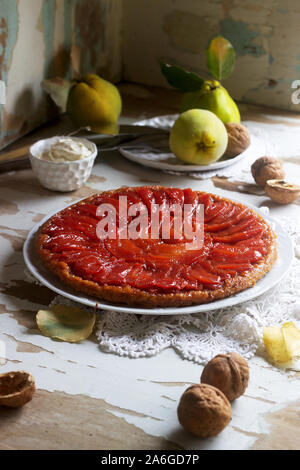 Quitte Tarte Tatin mit Schlagsahne, Quitte Obst und Walnüsse auf einer hölzernen Oberfläche serviert. Im rustikalen Stil. Stockfoto