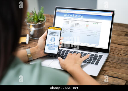Frau mit Handy App zu Authenthificate Banküberweisung auf Laptop Stockfoto