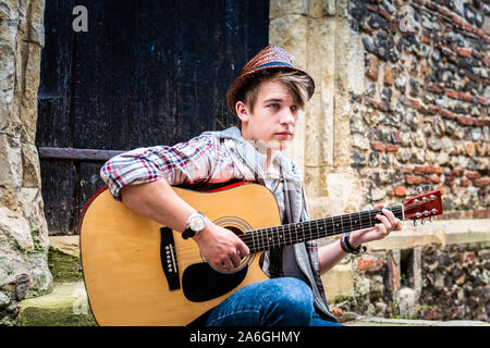 Ein hübscher junger Mann in einen Hut, Gitarre zu spielen und Straßenmusik für Geld Stockfoto