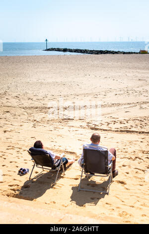 Zwei Männer sitzen am Strand die Sonne genießen, nicht weit von der Anlegestelle an einem warmen Tag im Mai Stockfoto