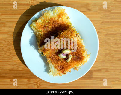 Traditionelle östliche Dessert kunafa. Blick von oben auf die arabische Käse kunafa in weiße Platte auf hellem Holztisch. Konafa. Stockfoto