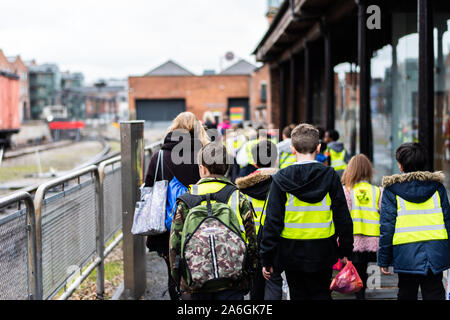 Eine Gruppe von Schulkindern zu Fuß auf der Straße auf Klassenfahrt tragen hohe Sichtbarkeit Jacken für Sicherheit Stockfoto