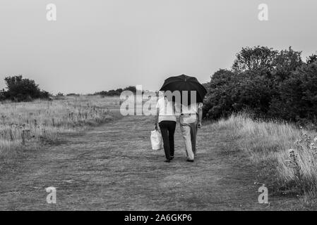 Ein älteres Ehepaar zu Fuß unter einem Sonnenschirm im Walton auf der Naze, Essex Stockfoto