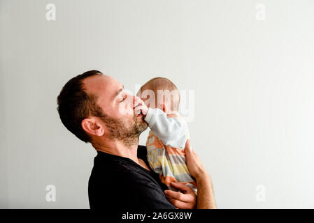 Seite Portrait von adorable Baby in den Armen seines Vaters sein Gesicht berühren mit seinen kleinen Händen, weißen Hintergrund. Stockfoto