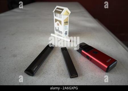 3 vapes Juul, Streben, Breeze, smok infinix mit einer Packung Marlboro Zigaretten und eine Zigarette draußen auf eine weiße strukturierte Tabelle gelegt, isoliert Stockfoto