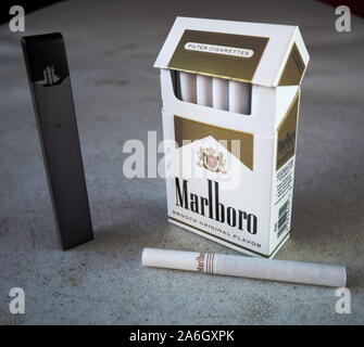 Juul vape Pod elektronische Zigarette Gerät mit einer Packung Marlboro Zigaretten und eine Zigarette draußen auf eine weiße strukturierte Tabelle gelegt, isoliert Stockfoto