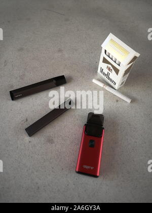 3 vapes Juul, Streben, Breeze, smok infinix mit einer Packung Marlboro Zigaretten und eine Zigarette draußen auf eine weiße strukturierte Tabelle gelegt, isoliert Stockfoto