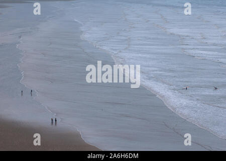 Die Menschen gehen am Strand entlang und genießen die Küste von Nord-Devon an einem kalten Wintertag. Die Aussicht ist riesig und lässt die Menschen winzig aussehen. Stockfoto