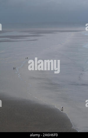 Die Menschen gehen am Strand entlang und genießen die Küste von Nord-Devon an einem kalten Wintertag. Die Aussicht ist riesig und lässt die Menschen winzig aussehen. Stockfoto