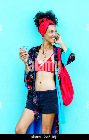 Afrikanische amerikanische Frau im Sommer Schal, ein rotes Top, mit ihrer Tasche abgestimmt, Musik hören mit Kopfhörern. Stockfoto