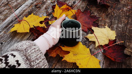 Linke Hand mit Handgelenk verzogen in einem Verband für eine Verstauchung und ein übergroßes Wollpullover Hülse, Halten einer Tasse auf einem rustikalen Holzmöbeln Herbst Hintergrund Stockfoto
