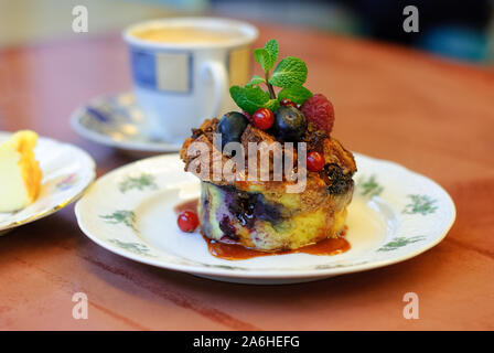 Ein schöner, frischer Kuchen mit Beeren, mit Minze in prächtigen Geschirr auf einen hölzernen Tisch serviert dekoriert. Berry Brotpudding. Stockfoto