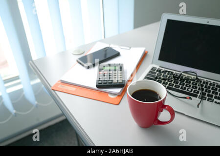 Anzeigen der Tabelle neben Windows mit Laptop. Fokus auf rote Kaffeetasse. Geschäft oder Arbeiten Konzept. Stockfoto