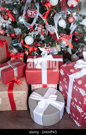 Boxen gebunden mit Bändern unter einem Weihnachtsbaum in roten Farben. Symbol für Glückwünsche und Geschenke für das Neue Jahr und Weihnachten. Stockfoto