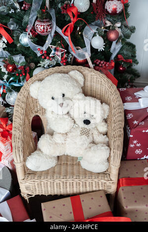 Weihnachtliche Stimmung, zwei weiße Spielzeug teddy vor dem Hintergrund einer geschmückten Weihnachtsbaum trägt. Warten auf ein Wunder, das Neue Jahr Dekorationen Stockfoto