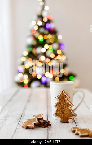 Frohe Weihnachten! Christmas Tree-förmige Lebkuchen Plätzchen in der Nähe von Tassen Tee. Schönen unscharfen Weihnachtsbaum Hintergrund mit leuchtende Girlande. Selecti Stockfoto