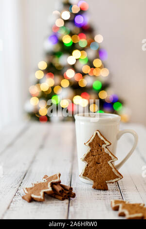 Frohe Weihnachten! Christmas Tree-förmige Lebkuchen Plätzchen in der Nähe von Tassen Tee. Schönen unscharfen Weihnachtsbaum Hintergrund mit leuchtende Girlande. Selecti Stockfoto