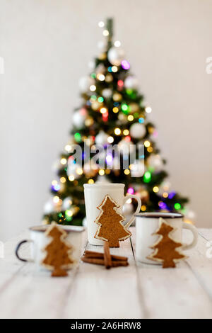 Frohe Weihnachten! Christmas Tree-förmige Lebkuchen Plätzchen in der Nähe von Tassen Tee. Schönen unscharfen Weihnachtsbaum Hintergrund mit leuchtende Girlande. Selecti Stockfoto