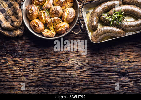 Gebratene Würstchen in der Pfanne mit Rosmarin und Kartoffeln.. Traditionelle europäische Küche Bratwurst oder jitrnice jaternice Stockfoto