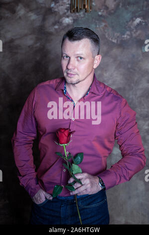 Angenehm weißer Mann mit einer roten Rose in der Hand, in die Kamera schaut, Porträt Stockfoto