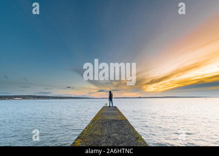 Mann stand auf Pier/Mole mit Blick auf das Meer bei Sonnenaufgang Stockfoto