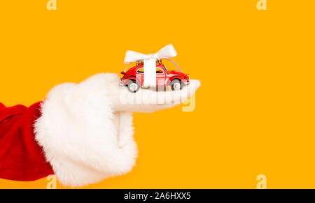 Santa Claus Holding modernes Auto mit Bogen in der Hand über Orange Stockfoto