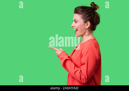 Hey Du! Seitenansicht Portrait von überrascht Mädchen mit bun Frisur, große Ohrringe und in rot Bluse Zeigefinger auf der linken Seite, mit Erstaunen. Stockfoto