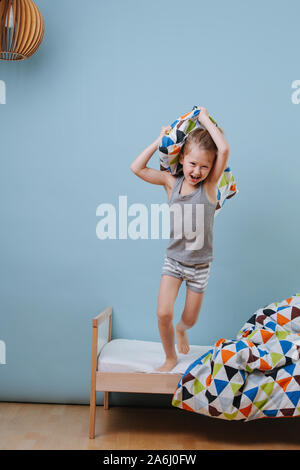 Kleiner Junge sprang vom Bett, bewaffnet mit einem Kissen über blaue Wände Stockfoto