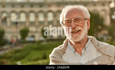 Es ist nie zu spät. Portrait von glücklich aussehenden Bärtigen älteren Mann in Gläsern an Kamera schauen und lächeln, während Sie die Zeit im Freien auf einer Stockfoto