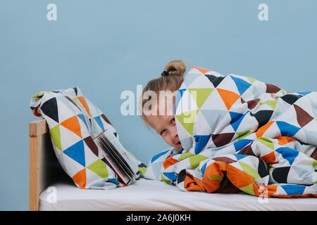 Kleiner Junge im Bett liegen und so tun, als zu lesen, bis seine Eltern verlassen Stockfoto