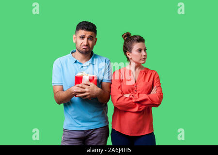 Portrait von wütend aufgebrachtes Frau in legere Kleidung stand mit verschränkten Armen, enttäuscht mit Geschenk, wandte sich von Mann hält schlecht. isol Stockfoto