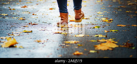 Spaziergang auf dem nassen Bürgersteig. Ansicht von hinten auf den Füßen einer Frau zu Fuß entlang der Asphalt mit Pfützen im Regen. Paar Schuh auf glatter Straße in t Stockfoto