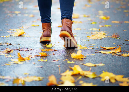 Spaziergang auf dem nassen Bürgersteig. Ansicht von hinten auf den Füßen einer Frau zu Fuß entlang der Asphalt mit Pfützen im Regen. Paar Schuh auf glatter Straße in t Stockfoto