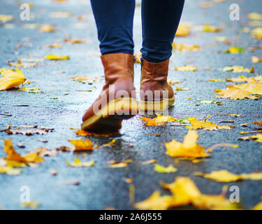 Spaziergang auf dem nassen Bürgersteig. Ansicht von hinten auf den Füßen einer Frau zu Fuß entlang der Asphalt mit Pfützen im Regen. Paar Schuh auf glatter Straße in t Stockfoto