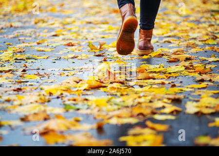 Spaziergang auf dem nassen Bürgersteig. Ansicht von hinten auf den Füßen einer Frau zu Fuß entlang der Asphalt mit Pfützen im Regen. Paar Schuh auf glatter Straße in t Stockfoto